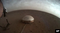 Na tym niedatowanym zdjęciu udostępnionym przez NASA w czwartek, 22 lipca 2021 r., chmury dryfują nad pokrytym kopułą sejsmometrem SEIS lądownika InSight na Marsie.