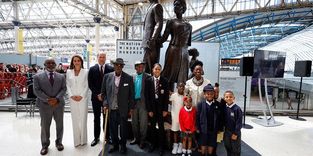 Książę William, Katarzyna, księżna Cambridge, baronowa Floella Benjamin, po prawej, pasażerowie Windrush Alford Gardner, pośrodku, John Richards, czwarty od lewej i dzieci przy Pomniku Narodowym Windrush stworzonym przez jamajskiego artystę Basila Watsona, po lewej, na stacji Waterloo w Londynie 22 czerwca 2022 r.