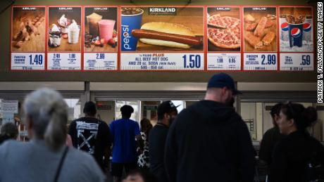 Klienci czekają w kolejce, aby zamówić poniższe tabliczki na zestaw Hot Dog i Soda za 1,50 USD od Costco Kirkland.