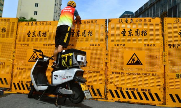 Kurier stojący na rowerze elektrycznym, który ma dostarczyć towary przez blokadę drogową w Sanya w prowincji Hainan